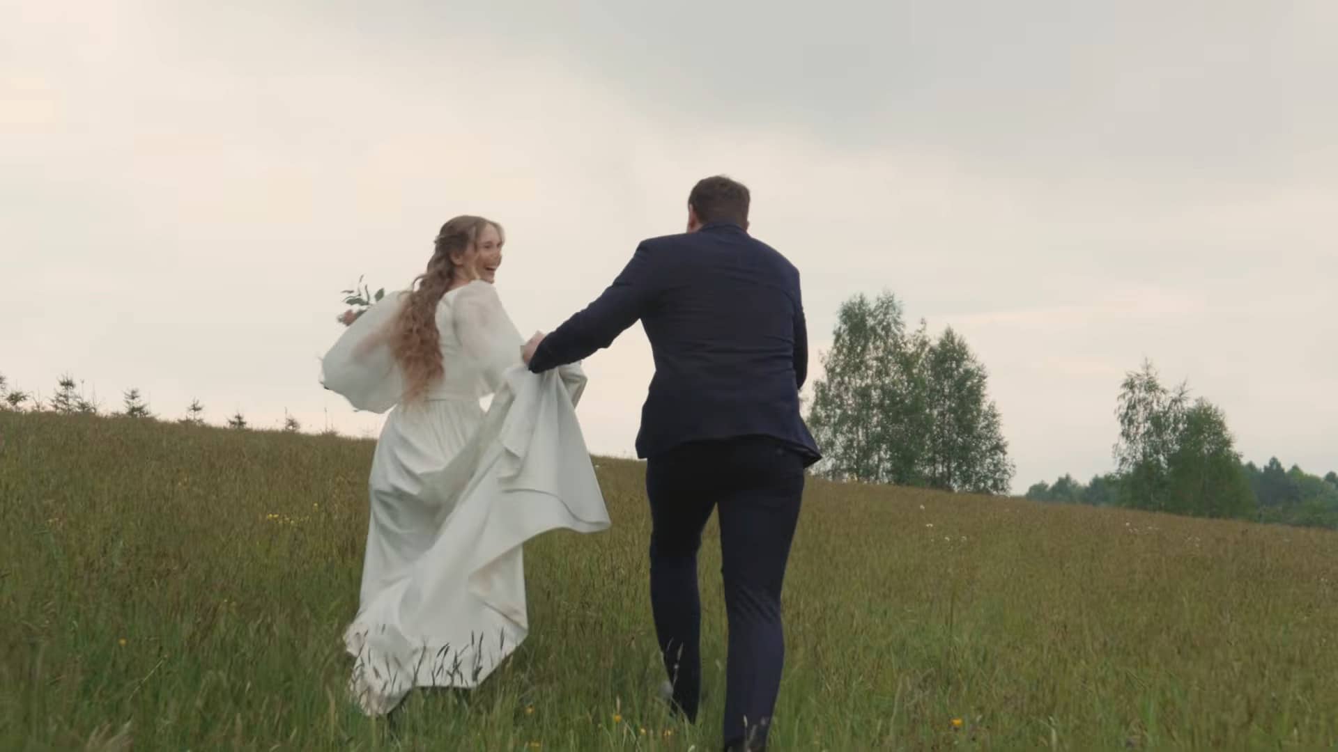 Das Brautpaar läuft Hand in Hand über eine weite Wiese, die Braut rafft ihr Kleid.