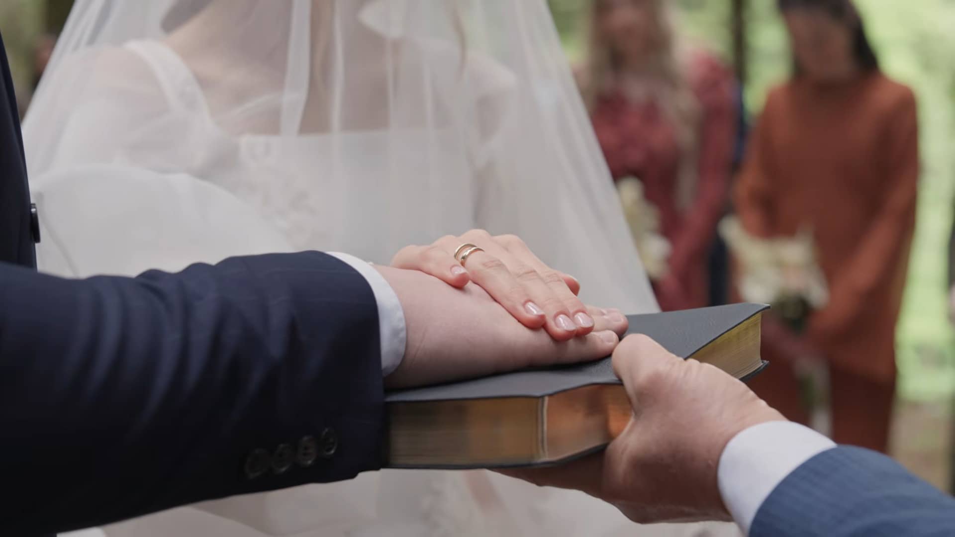 Die Hände des Brautpaares liegen mit ihren Ringen übereinander auf einer Bibel.